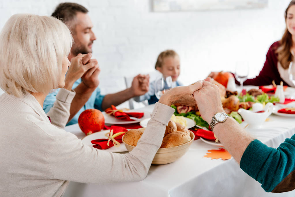 A family sitting at the Thanksgiving table holding each other's hands and giving thanks